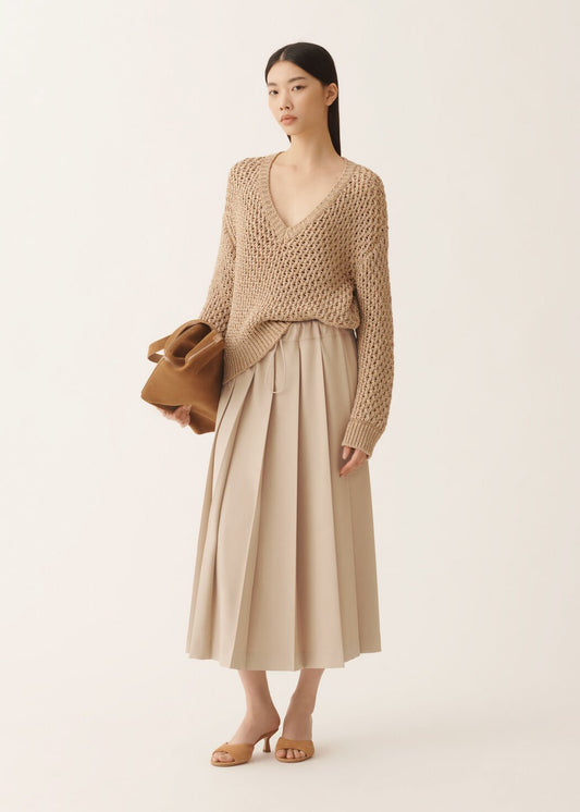 Woman wearing a beige knit sweater and skirt holding a brown bag on a white background
