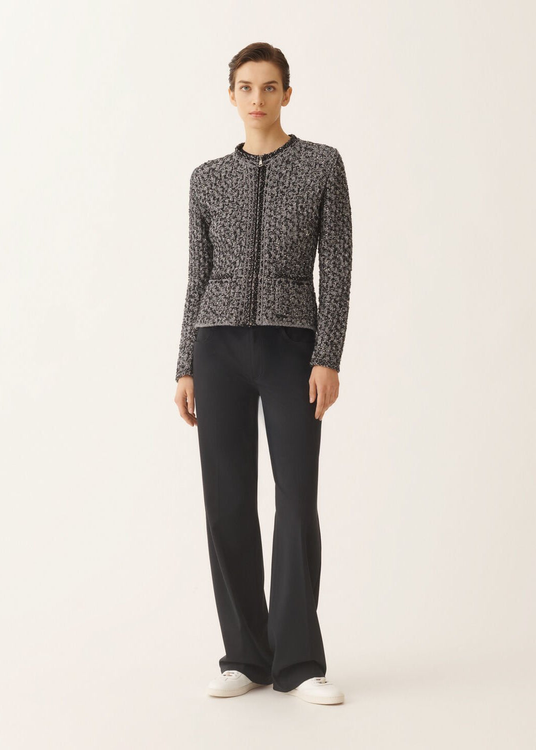 Woman wearing a patterned jacket and black pants on a white background