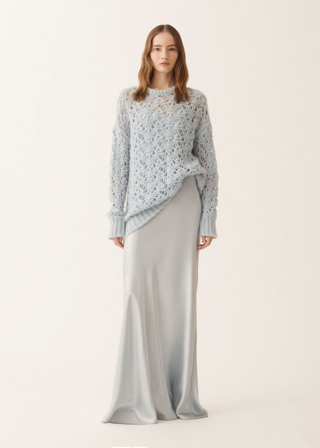 Woman wearing a light blue patterned top and white pants on a plain background