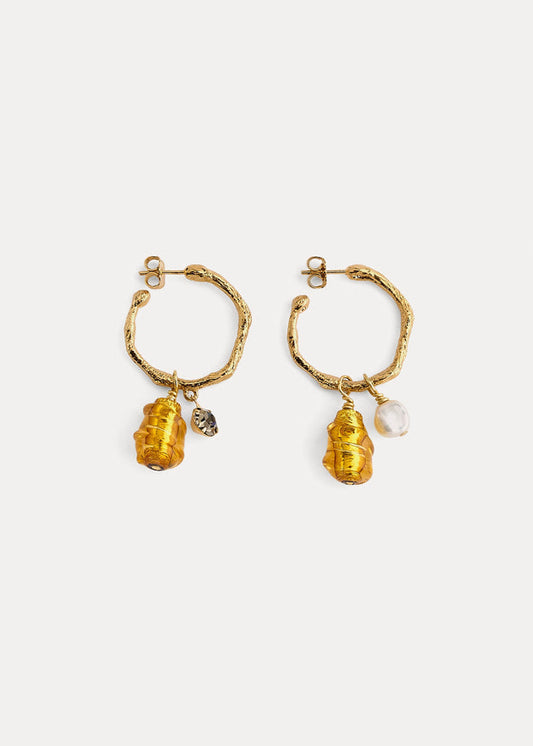 A pair of gold-toned textured hoop earrings with dangling organic-shaped amber-yellow beads and small clear stone charms, shown on a light gray background.