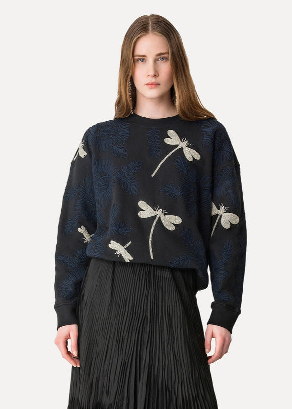 Woman wearing a dark sweater with dragonfly patterns on a white background