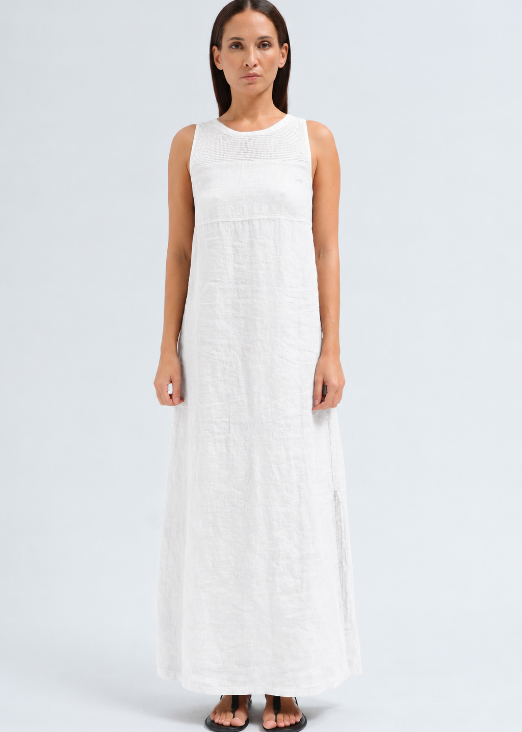 A woman modeling a sleeveless white linen maxi dress with a textured crinkle fabric, shown against a light gray studio background.