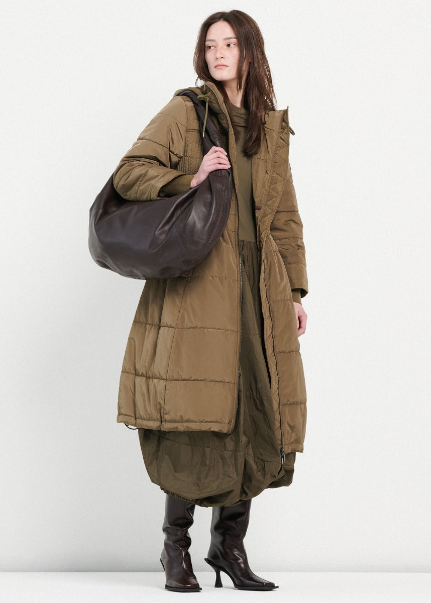 Woman wearing a long brown puffer coat holding a large brown bag on a white background