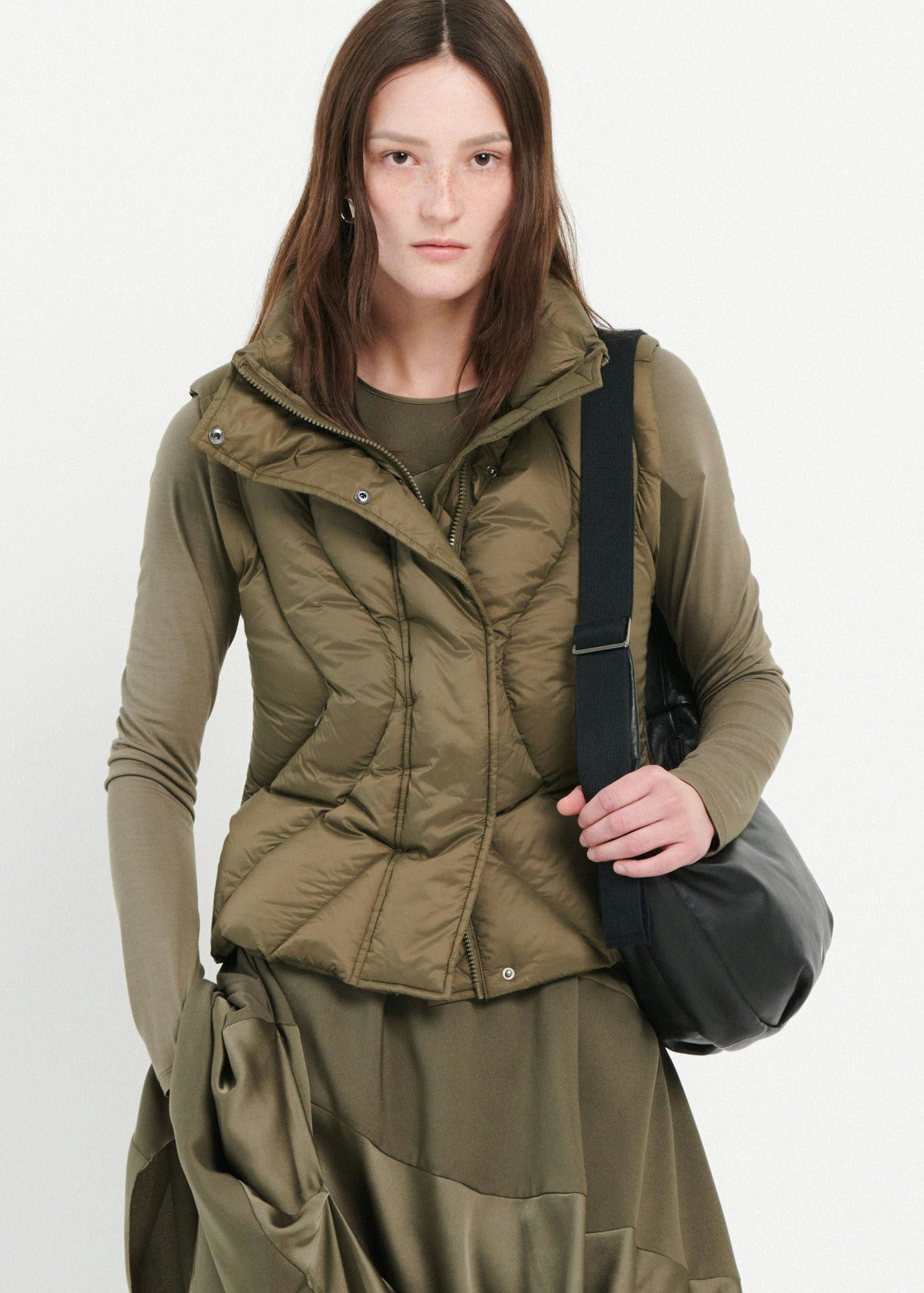 Woman wearing a green puffer jacket holding a black bag on a white background