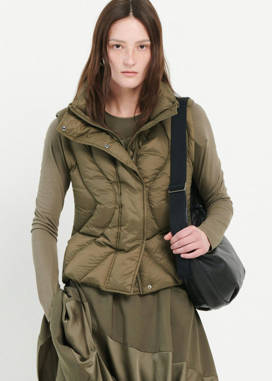 Woman wearing a green puffer jacket holding a black bag on a white background