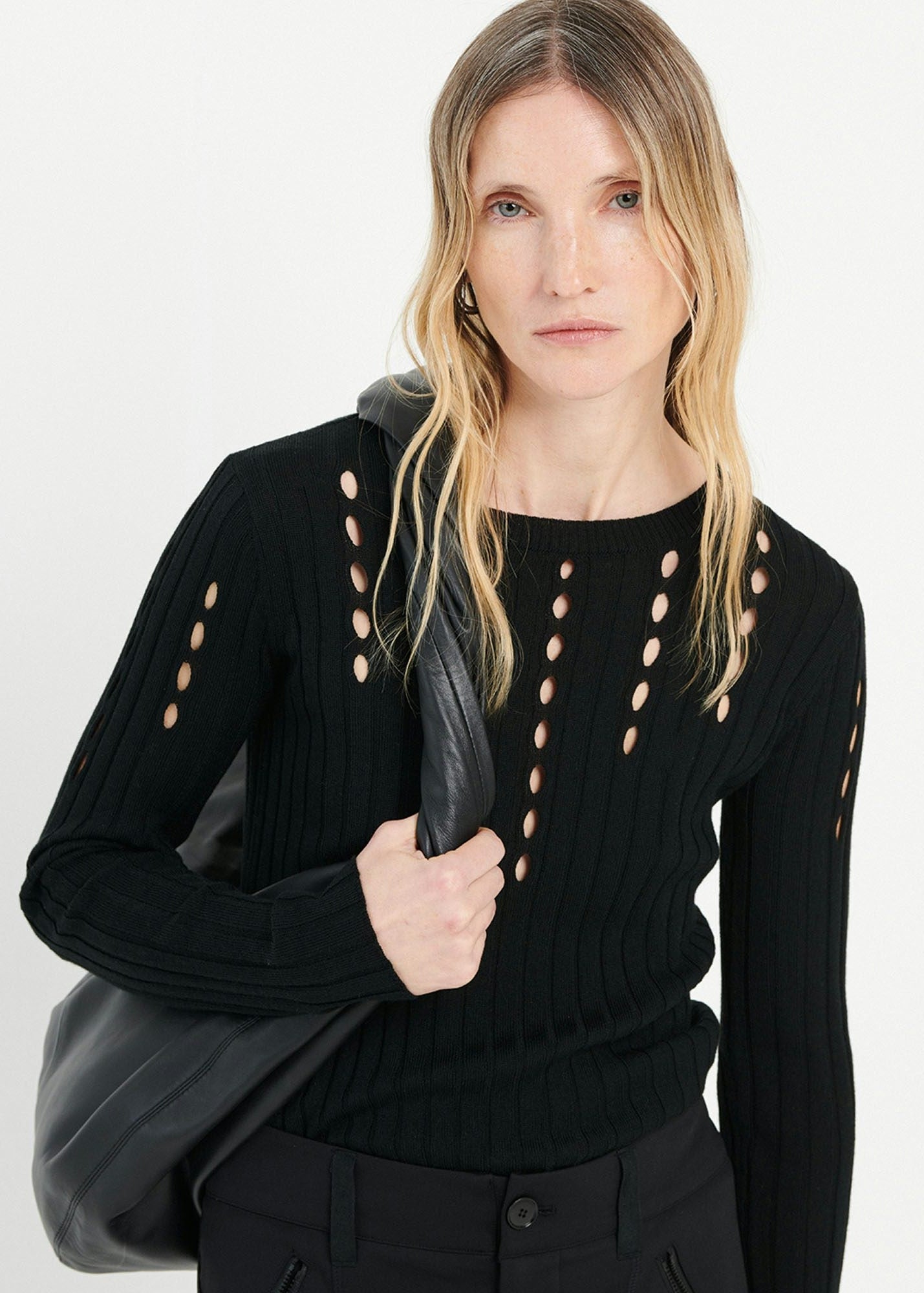 Woman wearing a black sweater with cut-out details on a white background