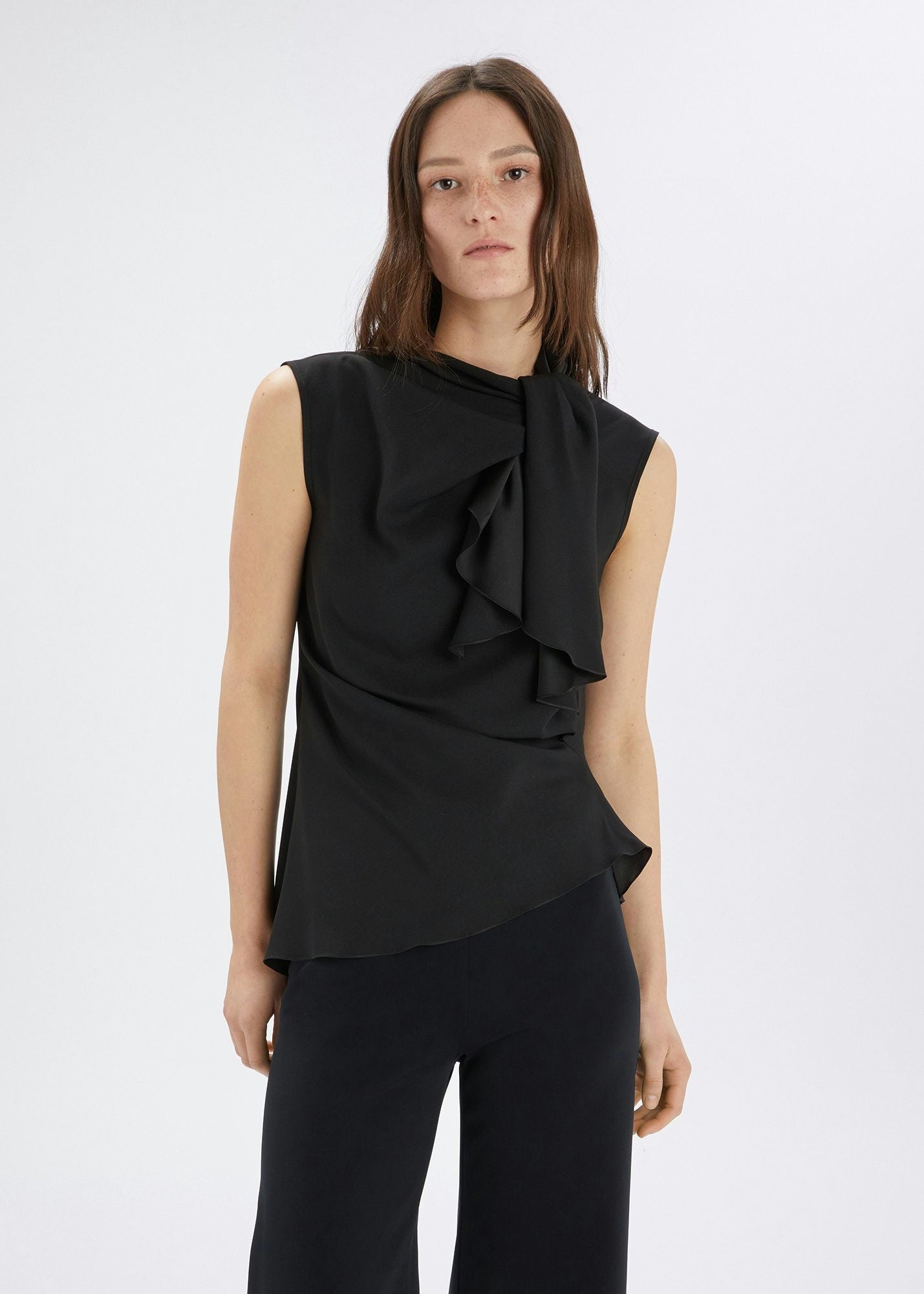 Woman wearing a black sleeveless top with ruffle details on a white background