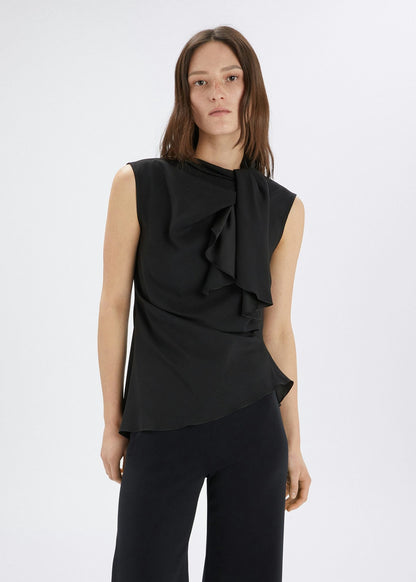 Woman wearing a black sleeveless top with ruffle details on a white background