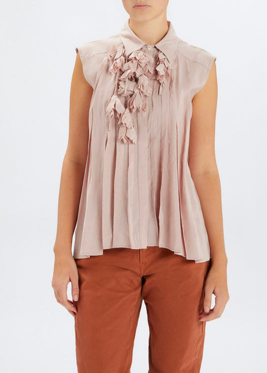 Woman wearing a beige sleeveless blouse with floral details and brown pants on a white background