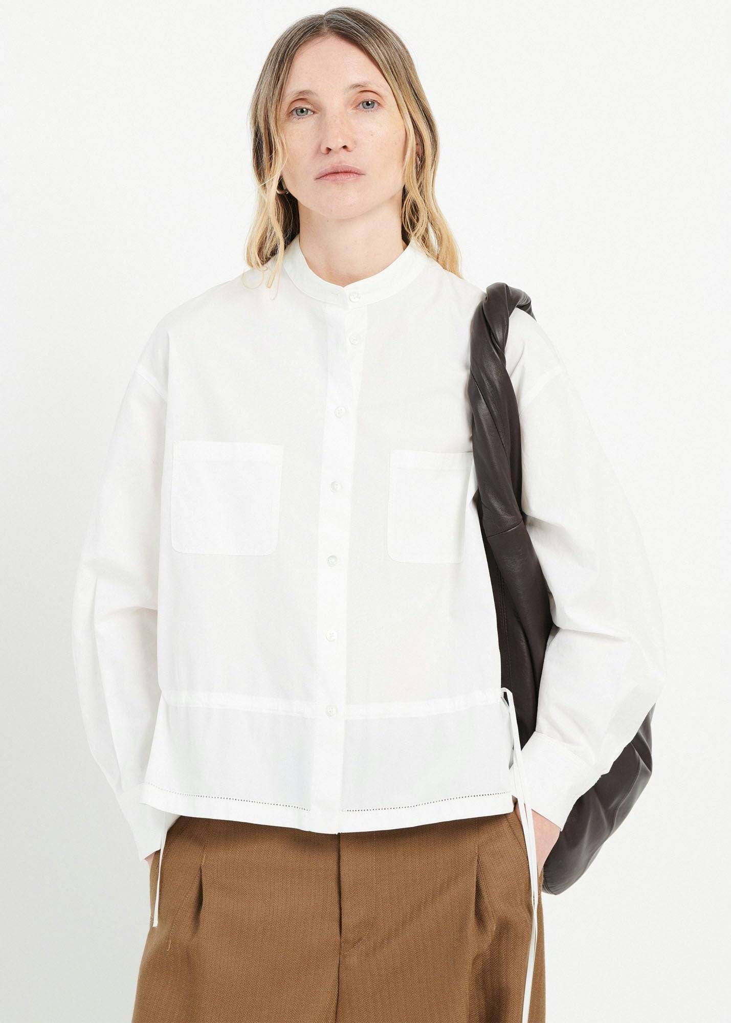 Person wearing a white shirt and brown pants with a black backpack on a white background
