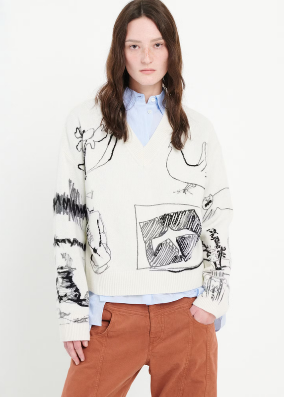 Person wearing a white sweater with black and gray abstract designs on a plain background