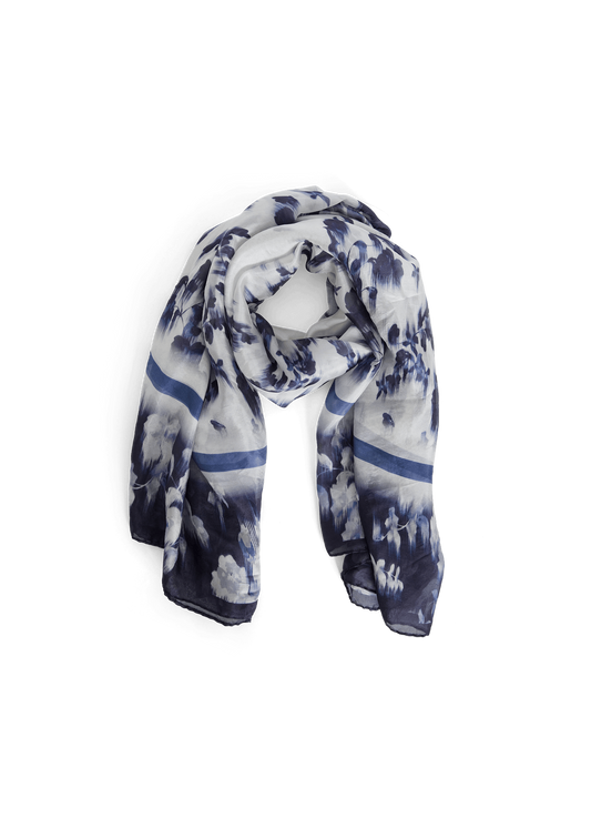 A lightweight scarf with a blue and white mountain landscape print, styled in a loop on a solid green background.