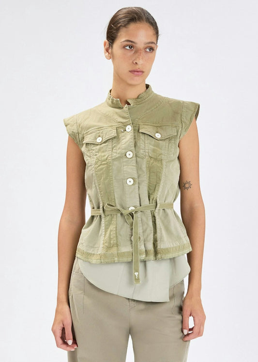 A woman modeling a sleeveless olive green cropped vest with a stand collar, front button closure, chest flap pockets, and a drawstring tie at the waist, paired with light olive pants against a plain light gray studio background.