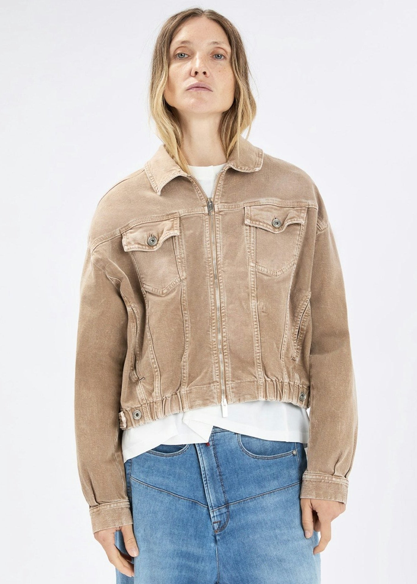 Person wearing a beige jacket and blue jeans on a white background