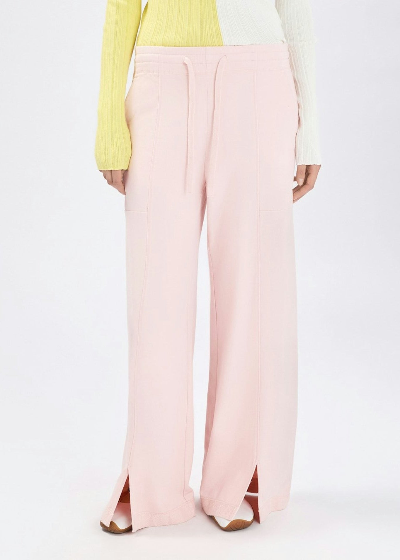 A model is shown from the back wearing light pink wide-leg trousers with side slits, styled with a yellow and white long-sleeve top against a plain white studio background.
