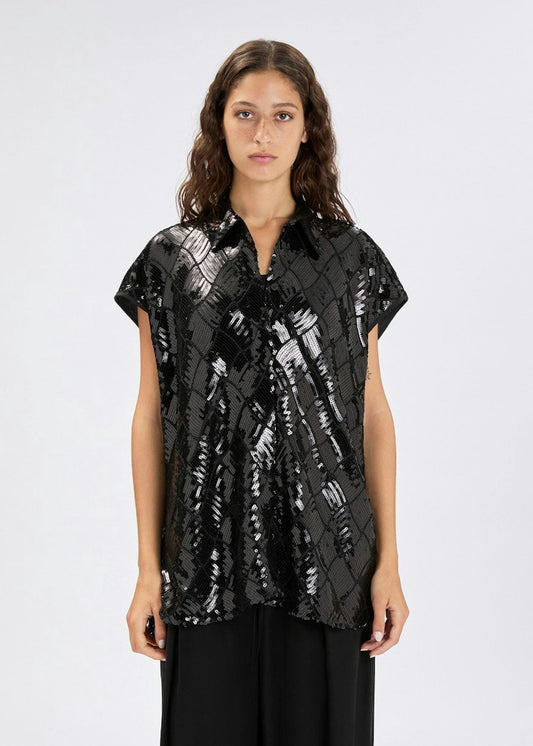 A woman modeling a black short-sleeve button-up shirt with a metallic silver abstract pattern, paired with black trousers, against a plain light gray background.