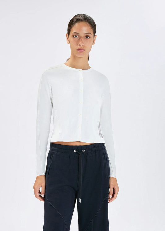 A model wearing a white long-sleeve cropped knit top and dark navy drawstring sweatpants, standing against a plain white studio background.