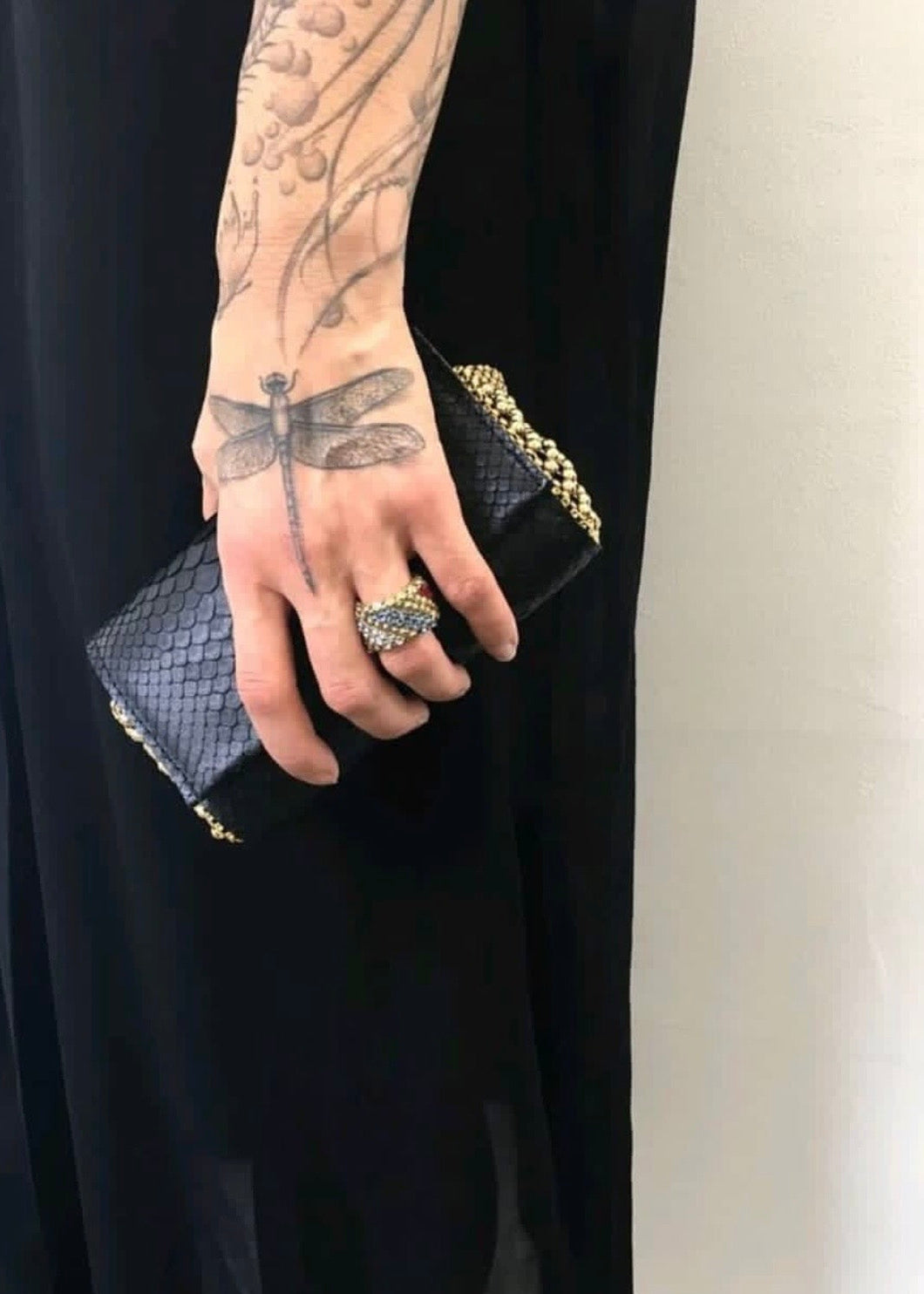 Hand holding a black clutch with gold accents against a neutral background