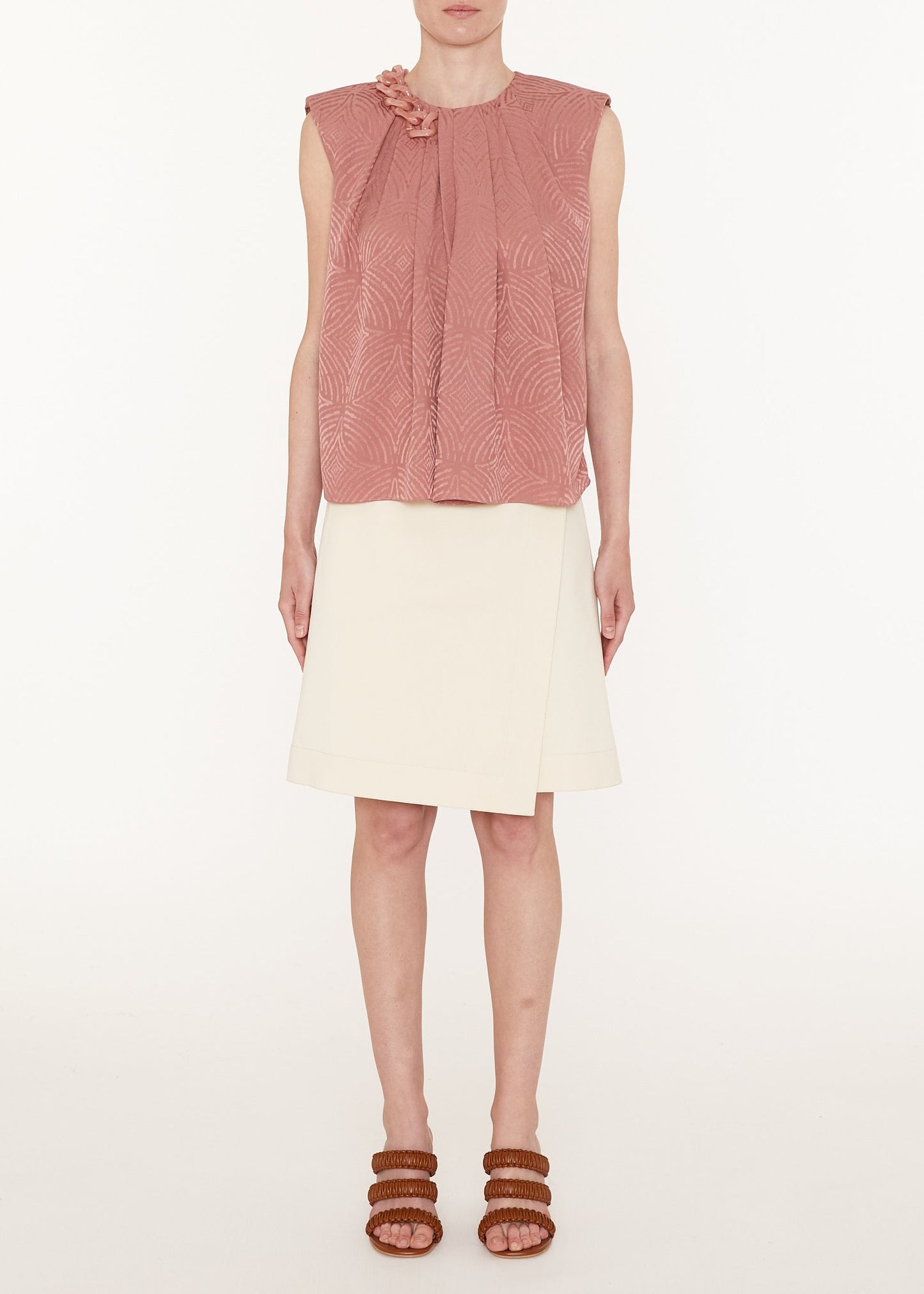 Woman wearing a pink sleeveless top and white skirt on a white background