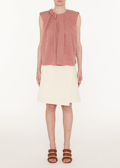 Woman wearing a pink sleeveless top and white skirt on a white background