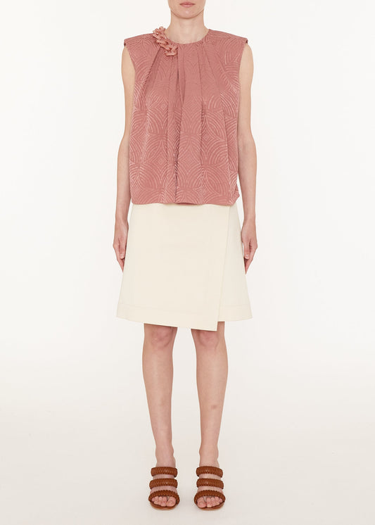 Woman wearing a pink sleeveless top and white skirt on a white background