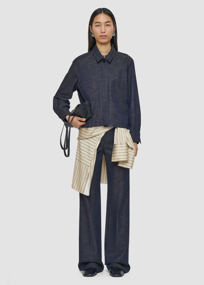 Person wearing a dark denim outfit with a beige pleated skirt on a white background