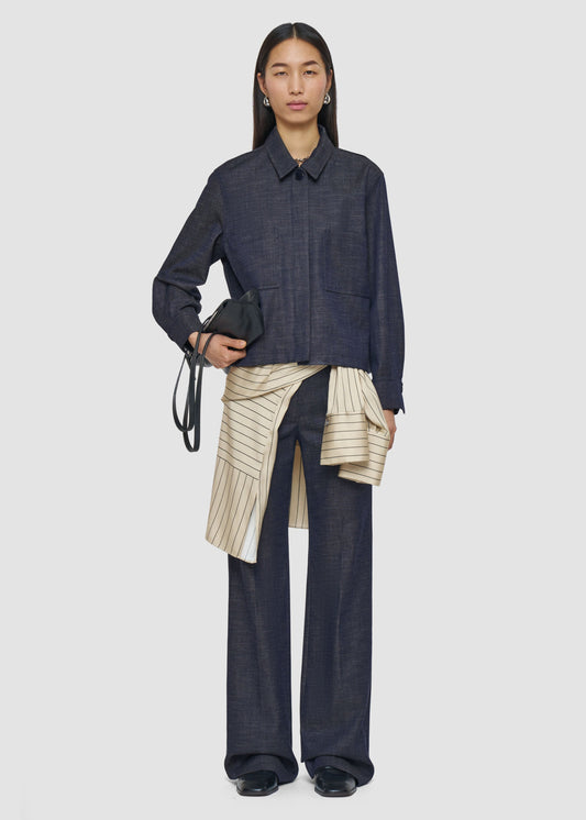 Person wearing a dark denim outfit with a beige pleated skirt on a white background