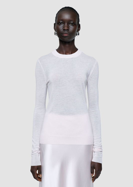 Person wearing a light gray sweater and white pants on a plain background