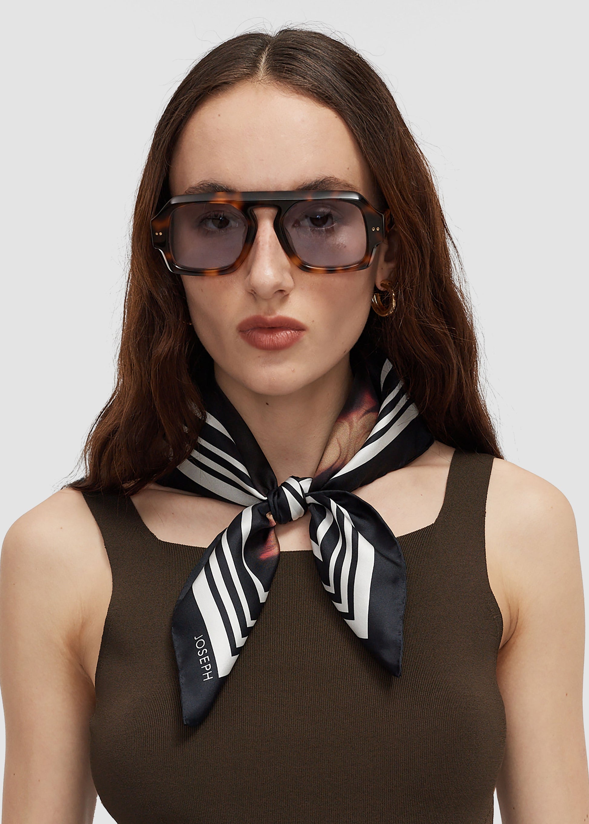 Woman wearing a black and white striped scarf with a brand logo, against a plain background