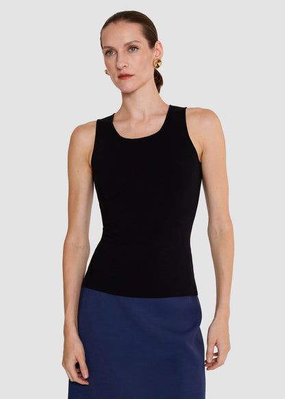 A woman modeling a black sleeveless scoop-neck top paired with a navy blue skirt, photographed against a solid light gray background.