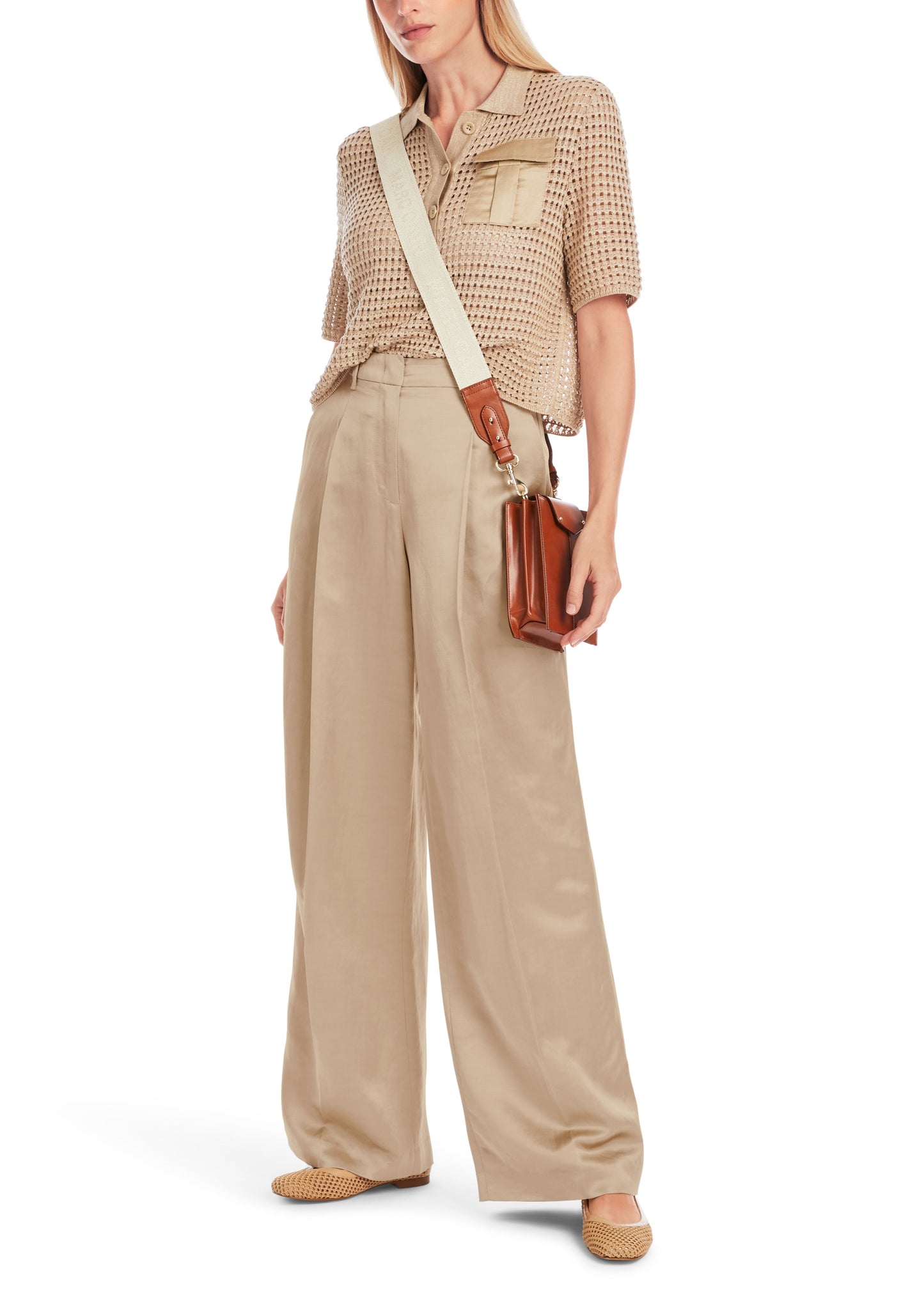 Woman wearing a beige patterned blouse and wide-leg pants, holding a brown leather bag.