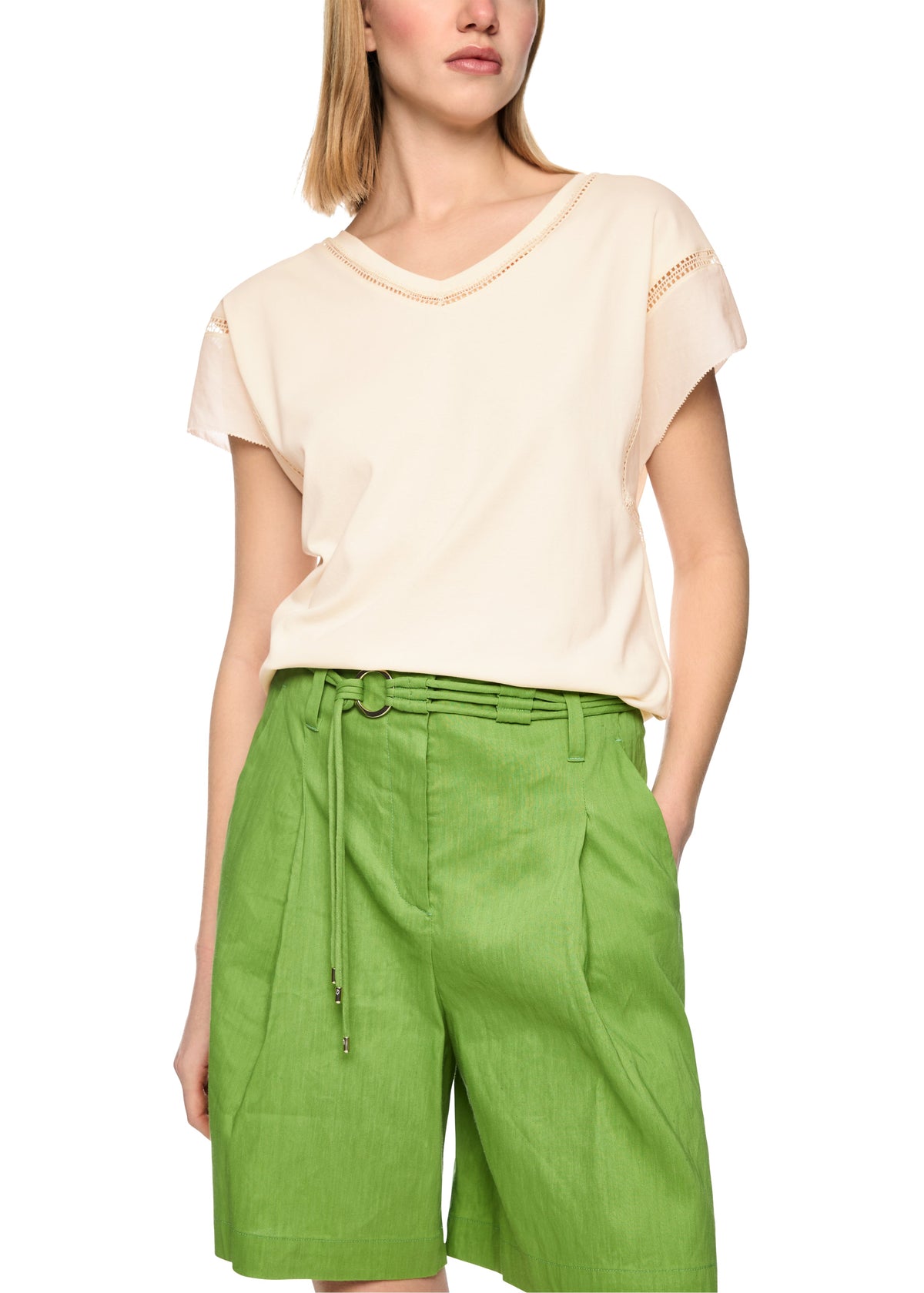 Woman wearing a beige top and green shorts on a white background