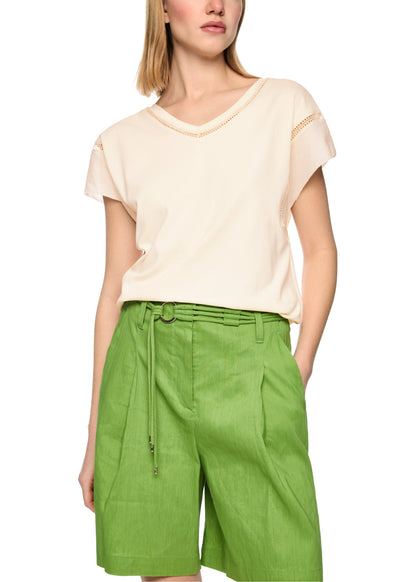 Woman wearing a beige top and green shorts on a white background