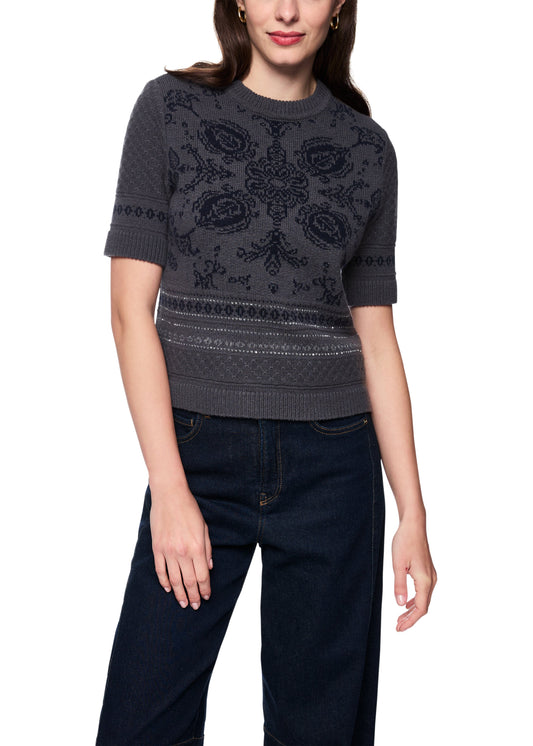 Woman wearing a dark gray patterned sweater and dark jeans on a white background