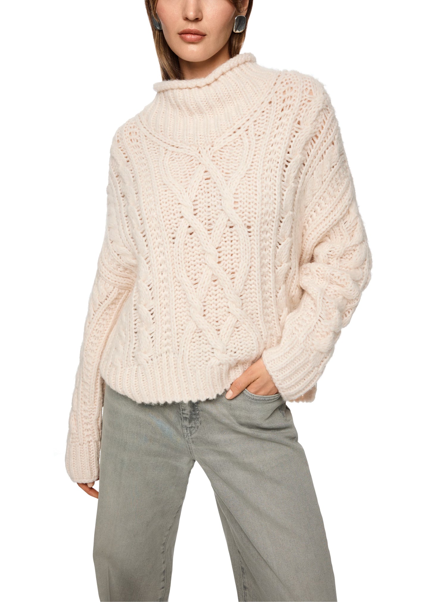 Person wearing a cream chunky knit sweater and light gray pants on a white background