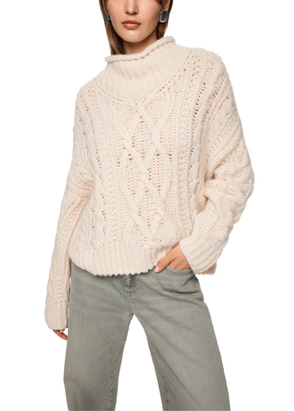 Person wearing a cream chunky knit sweater and light gray pants on a white background