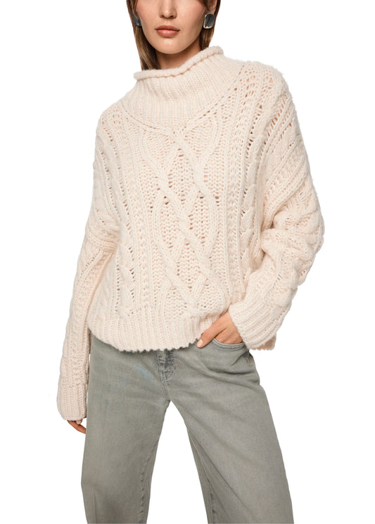 Person wearing a cream chunky knit sweater and light gray pants on a white background