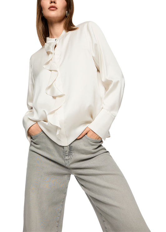 Person wearing a white blouse with ruffled details and light gray pants on a white background