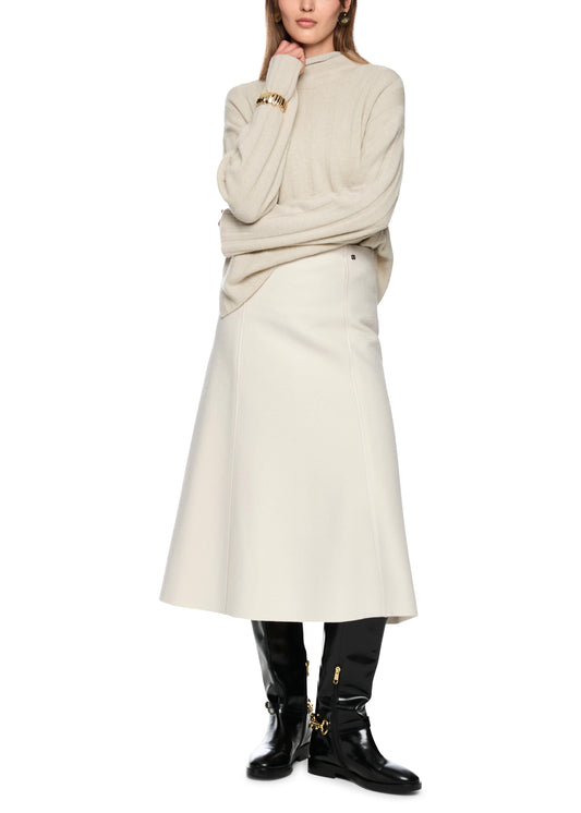 Person wearing a beige sweater and white skirt with black boots on a white background
