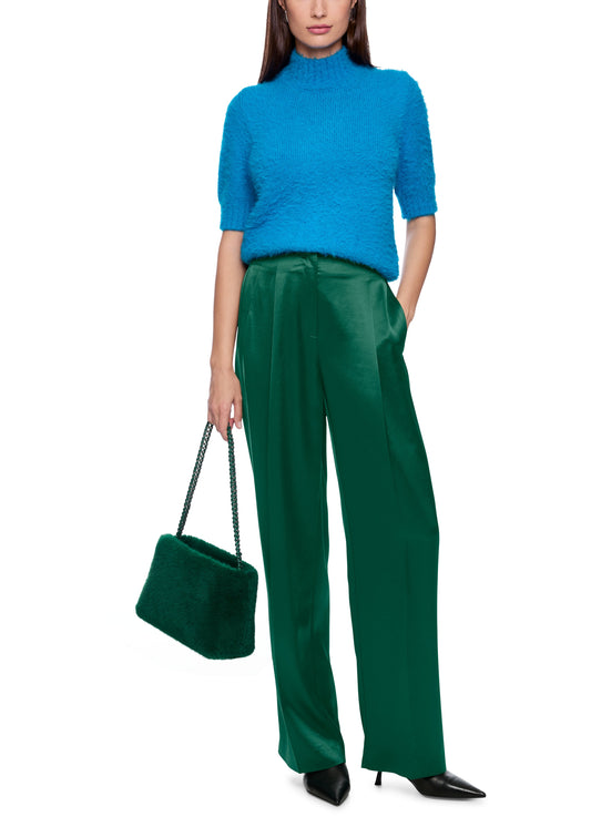 Woman wearing a blue sweater and green pants holding a green handbag on a white background