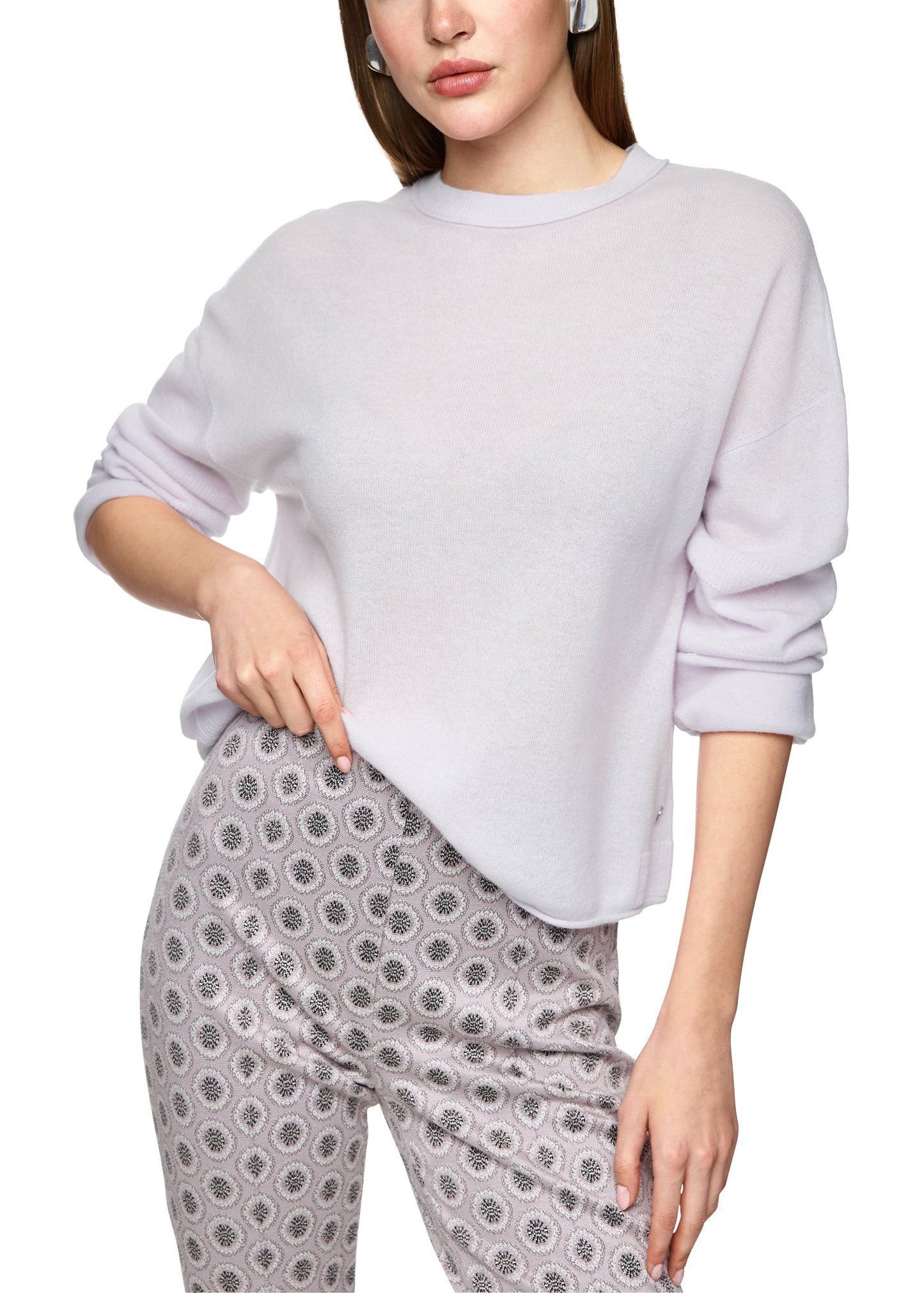 Woman wearing a light gray sweatshirt and patterned pants on a white background