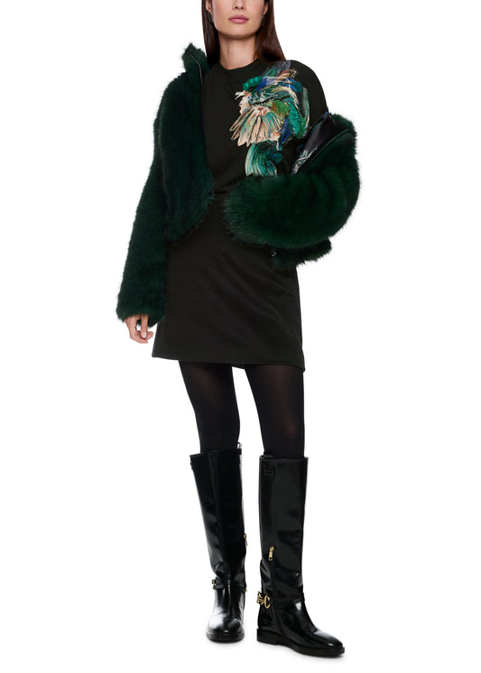 Person wearing a dark green fur coat, black dress, and black boots on a white background