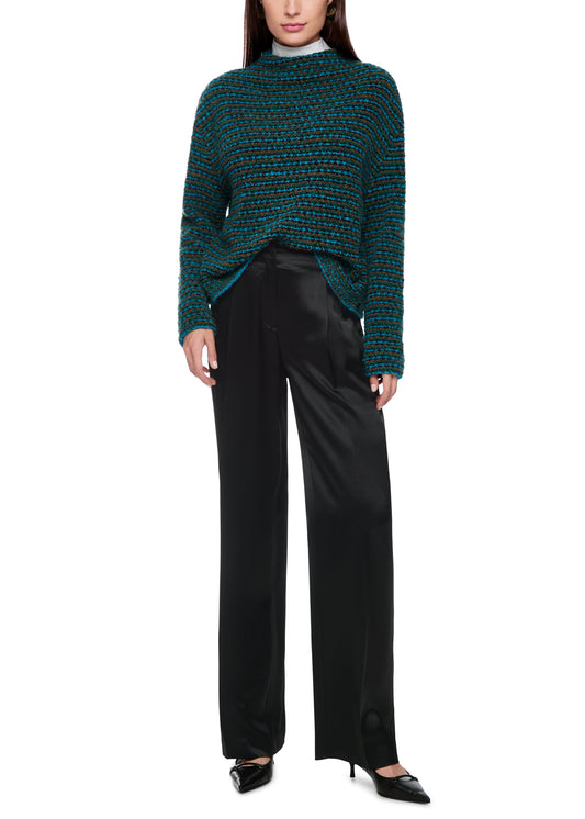 Woman wearing a green patterned sweater and black pants on a white background