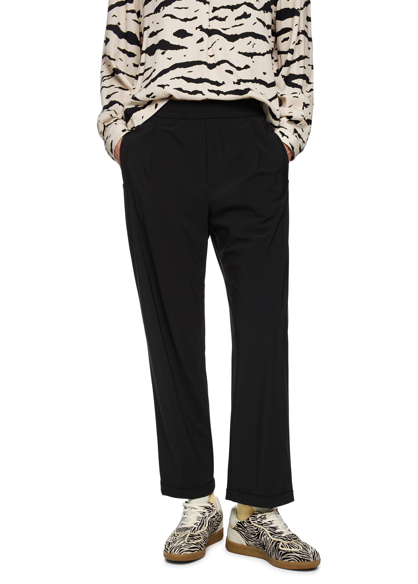 Person wearing a patterned sweater and black pants on a white background