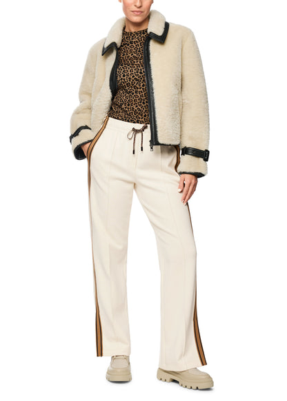 Person wearing a beige shearling jacket, leopard print top, and white pants on a white background
