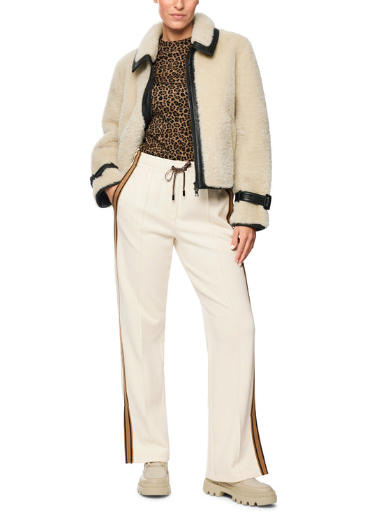 Person wearing a beige shearling jacket, leopard print top, and white pants on a white background