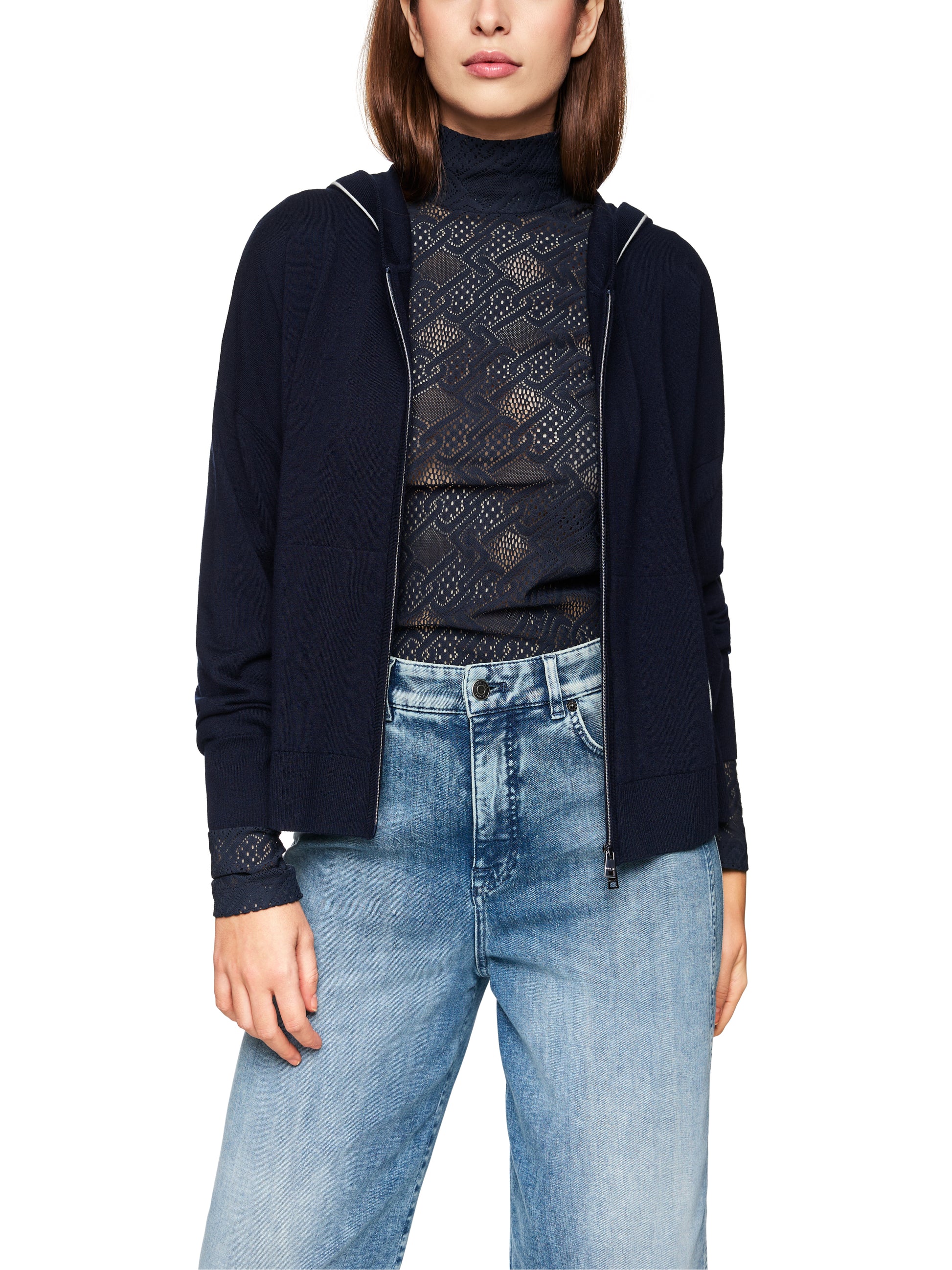 Woman wearing a navy cardigan, black lace top, and blue jeans on a white background