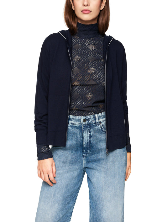 Woman wearing a navy cardigan, black lace top, and blue jeans on a white background