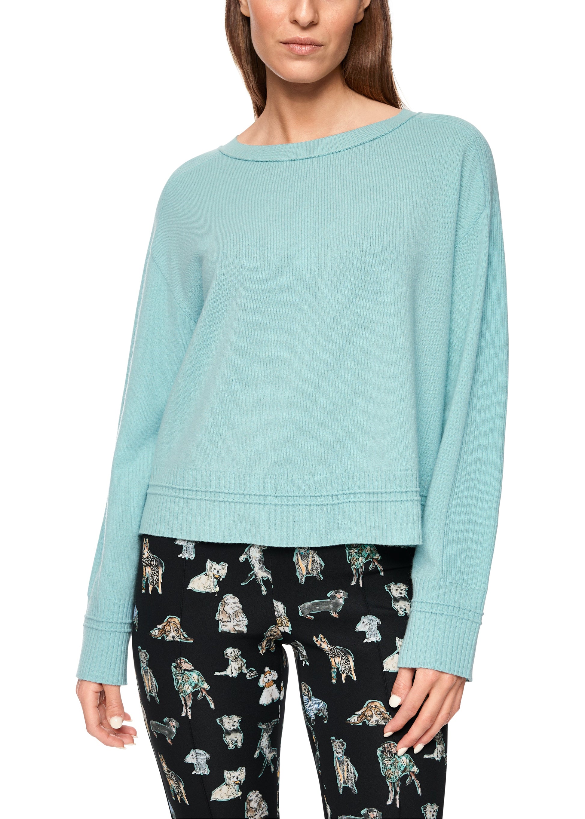 Woman wearing a light blue sweater and patterned pants on a white background