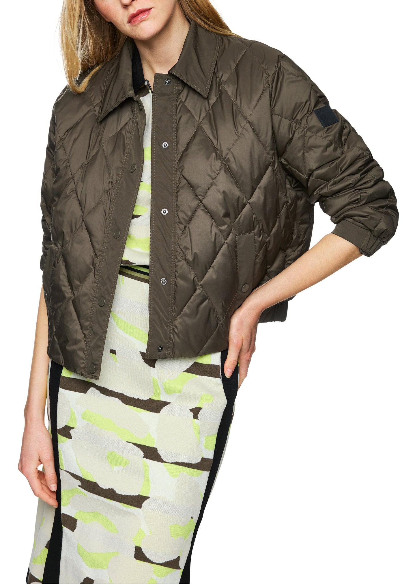 Person wearing a quilted jacket over a patterned dress on a white background